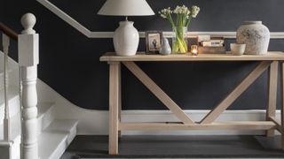 Dark grey painted hallway with natural wooden hallway console table with white ceramic lamp