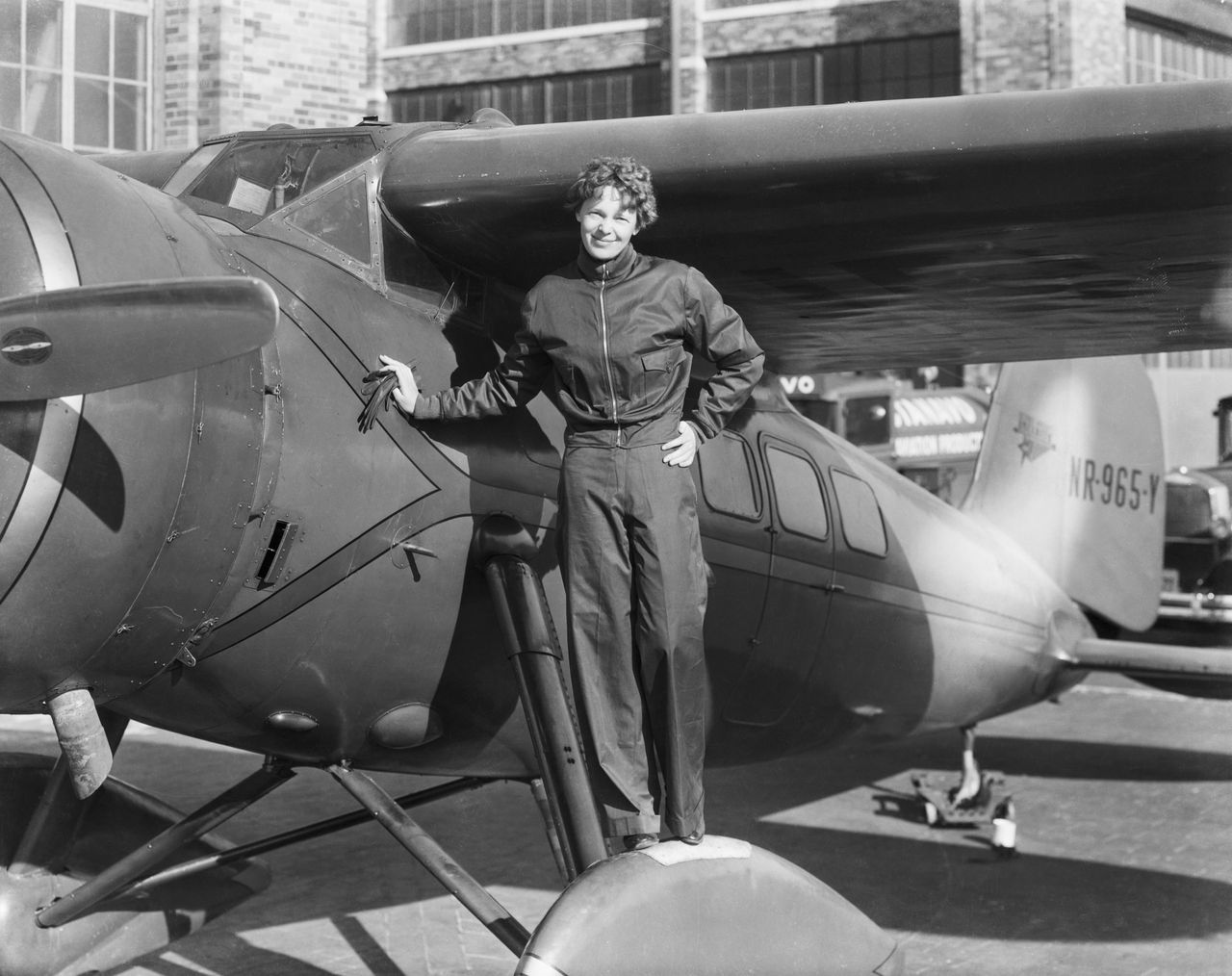 Amelia Earhart stands in front of a plane