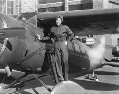 Amelia Earhart stands in front of a plane