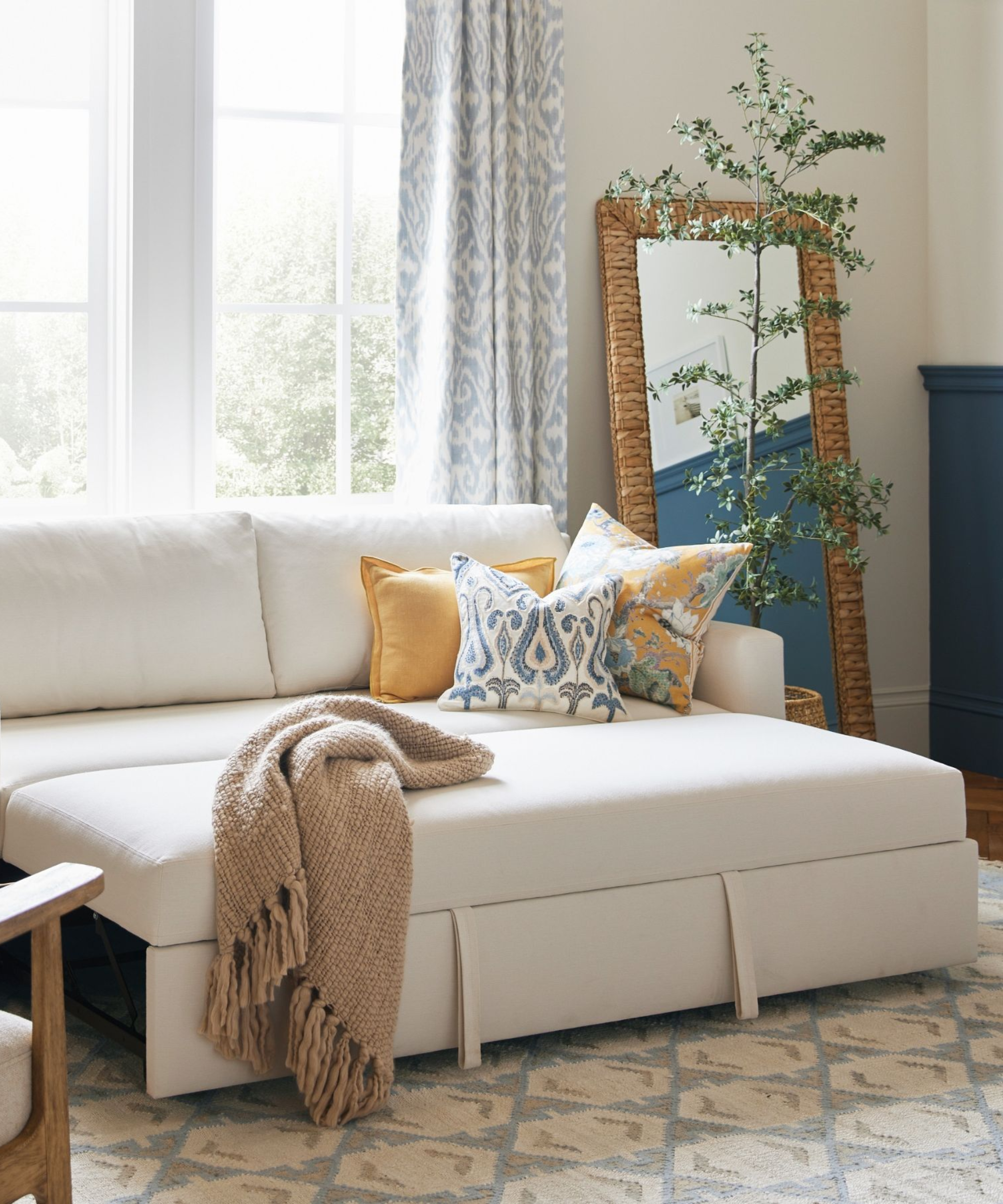 White Pottery Barn trundle sleeper sofa styled in a bright, bohemian living room with patterned throw pillows and a coordinating rug.