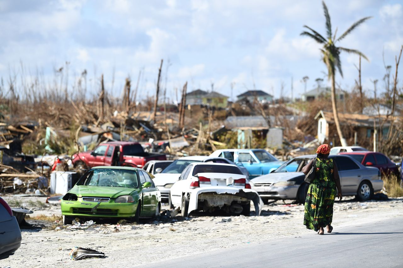 A woman walks by destroyed cars in Bahamian neighbourhood