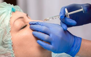 A stock photo of a woman receiving a "liquid nose job," a cosmetic procedure in which injections of facial fillers are used to change the appearance of the nose.