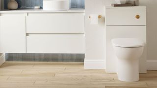 White toilet surrounded by white cabinets and wood-effect tiles on the floor