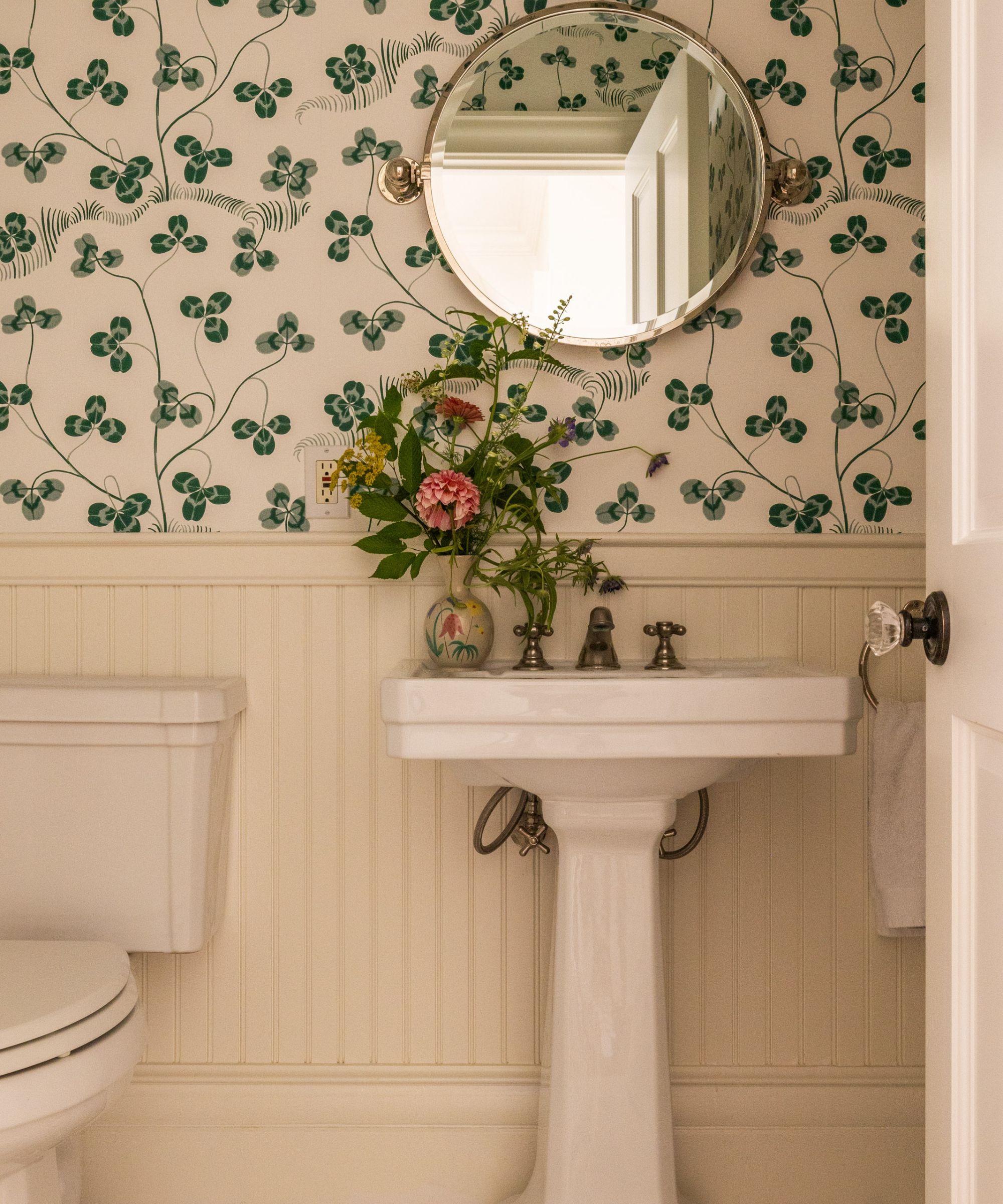 Bathroom with wood paneling, pedestal sink and green clover wallpaper