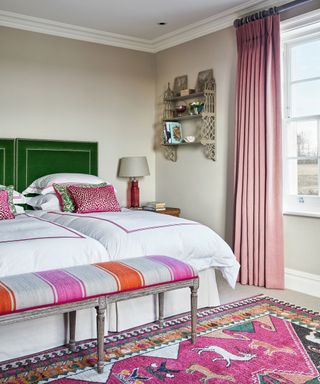 An example of bedroom curtain ideas showing a bedroom with pink drapes and green velvet headboards on twin beds