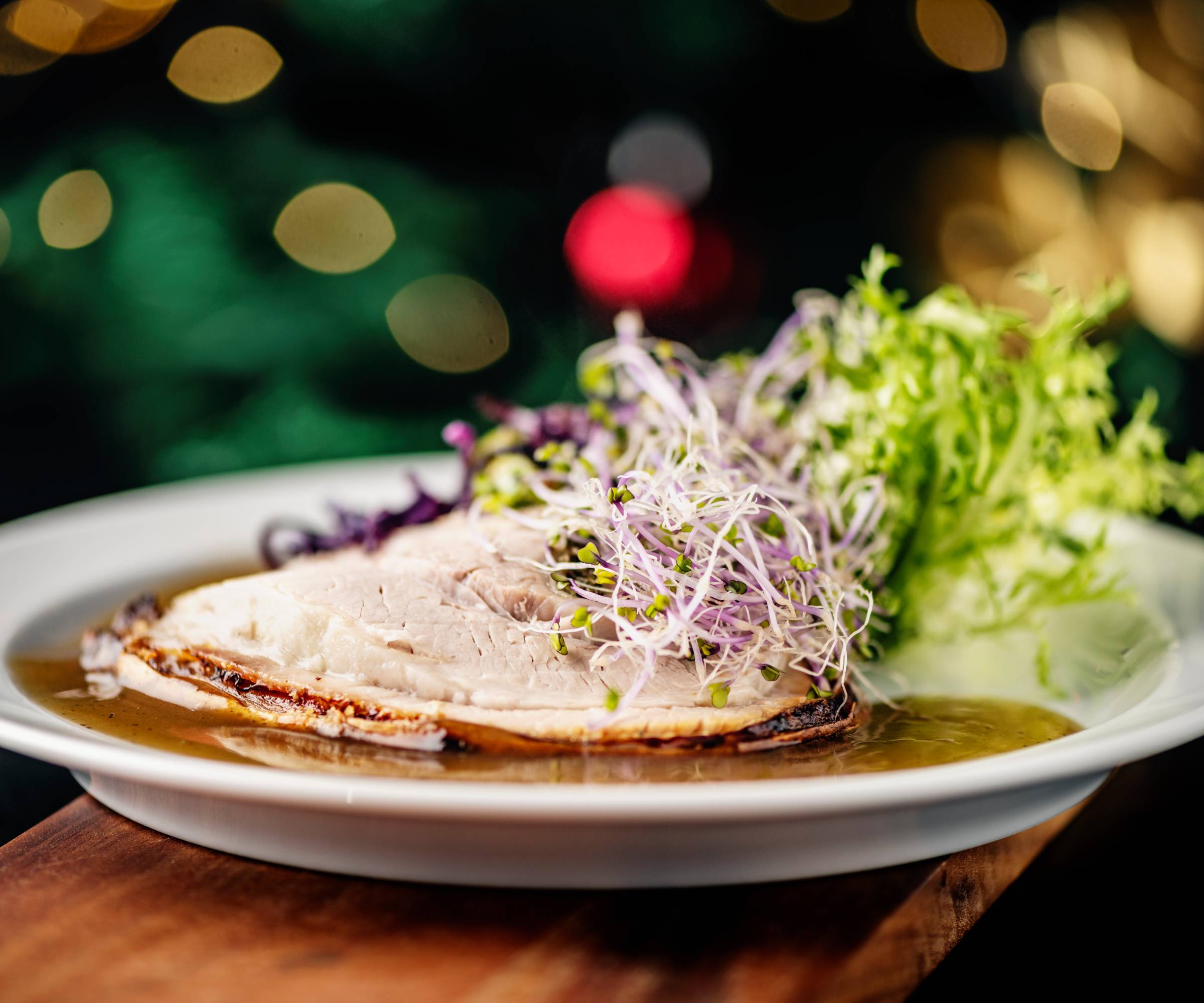 Microgreens on a slice of meat with gravy on a white plate