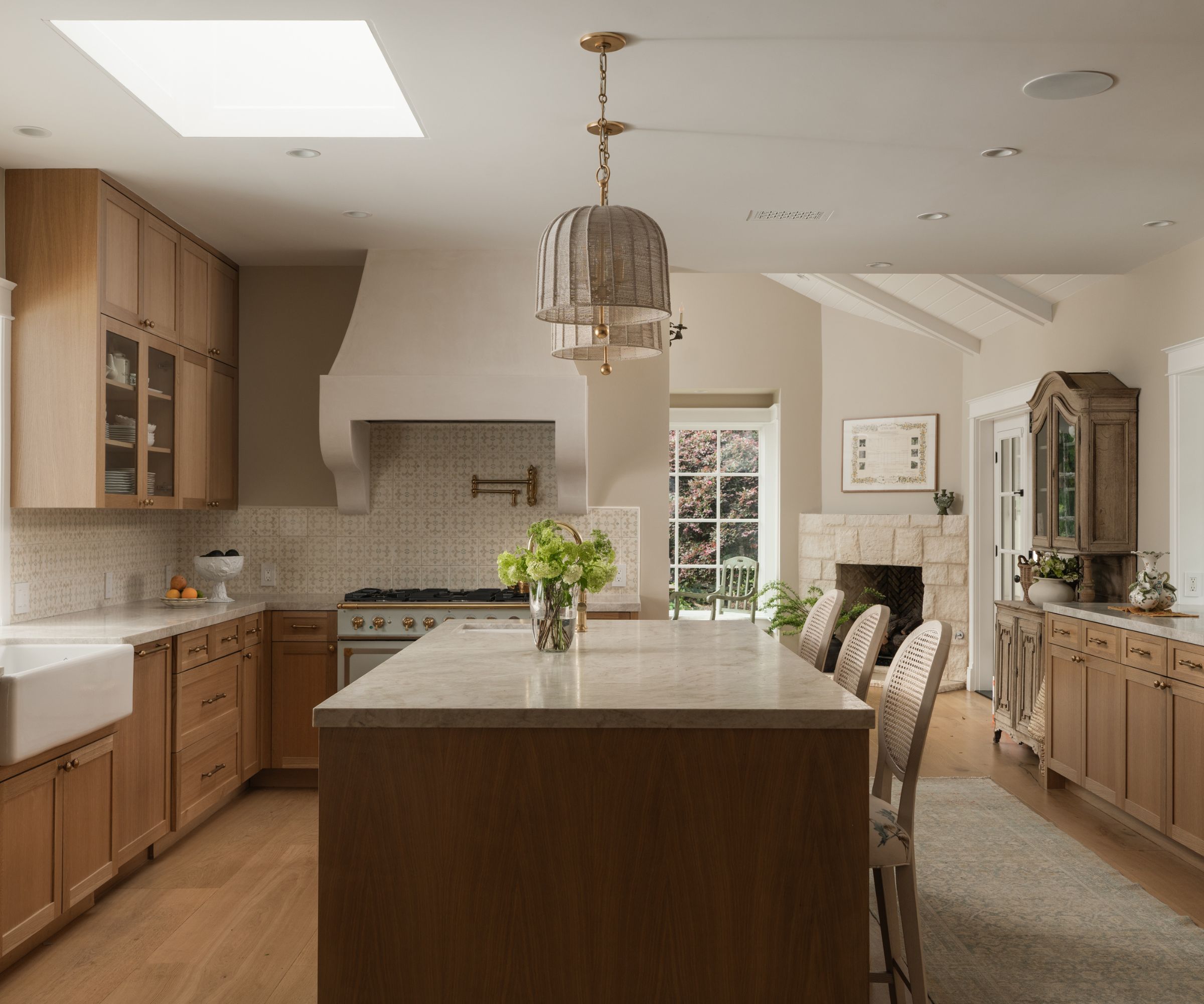 A large kitchen with mid-tone wood cabinets, light wood flooring, and a dark wood island