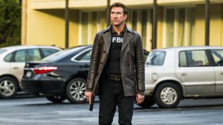 Dylan McDermott as Supervisory Special Agent Remy Scott in a leather coat with a gun in FBI: Most Wanted season 5