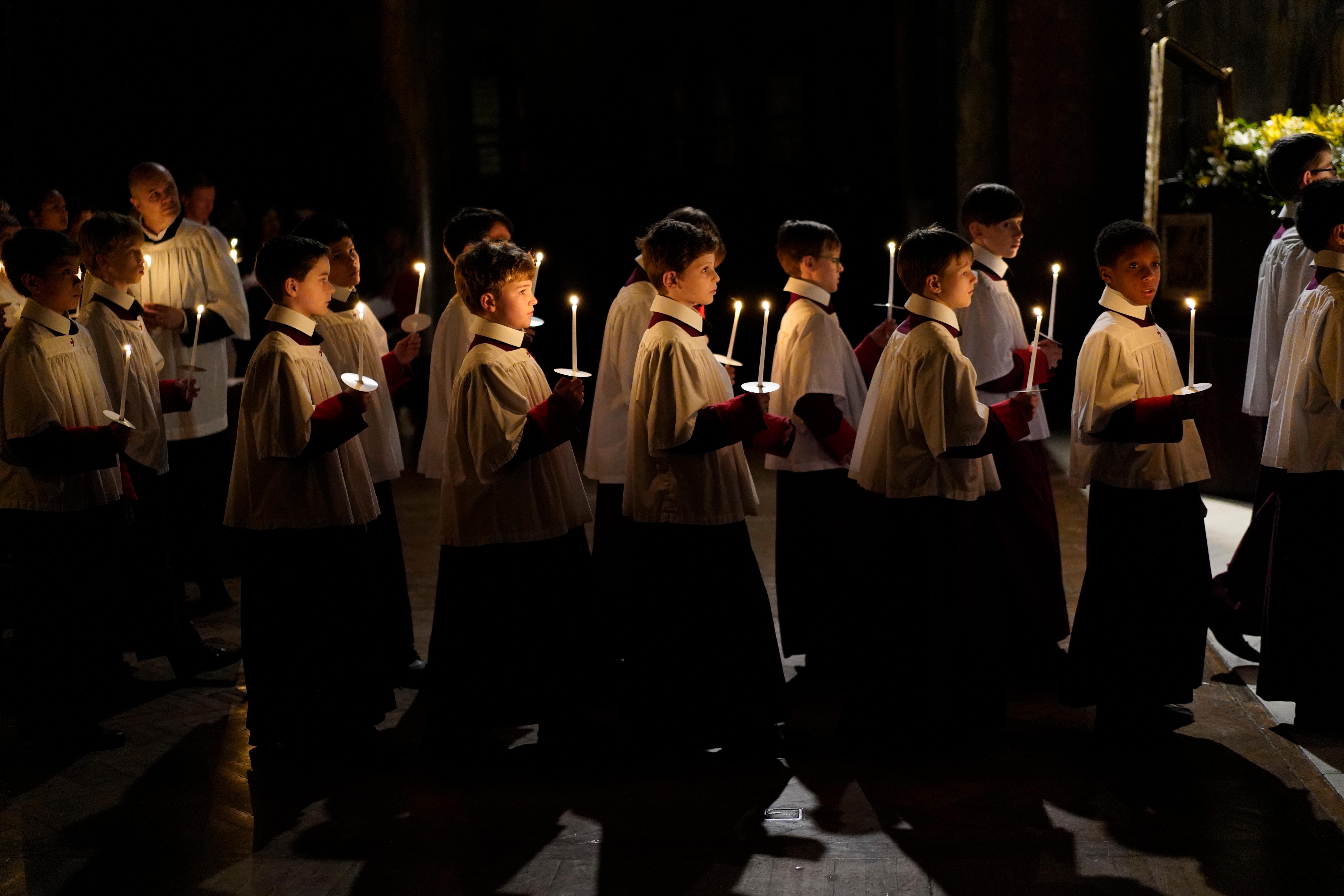 Choristers walk down the aisle of a church holding thin taper candles 