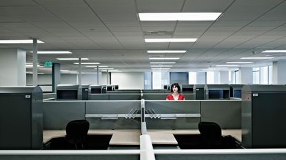 Businesswoman standing alone at cubicle in empty office