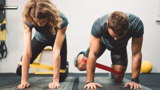 Man and woman perform fire hydrant exercise using resistance bands