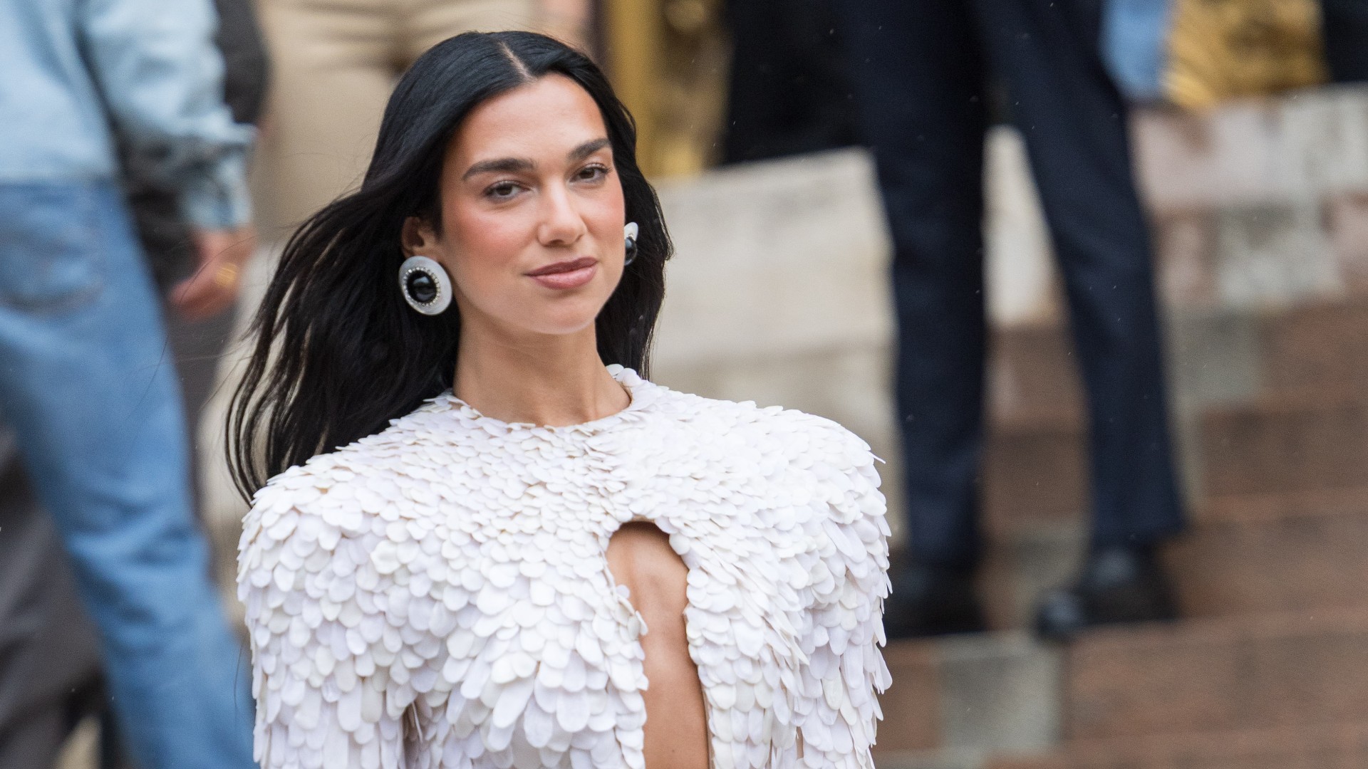 a paparazzi photo of a woman with long, black hair wearing a frilly white pantsuit