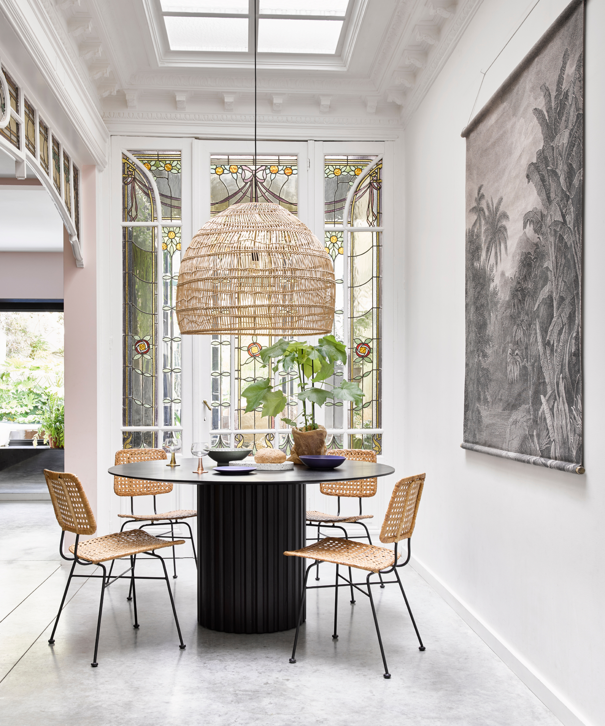 Dining area with high ornate ceiling, roof light, large rattan pendant light above round table and chairs