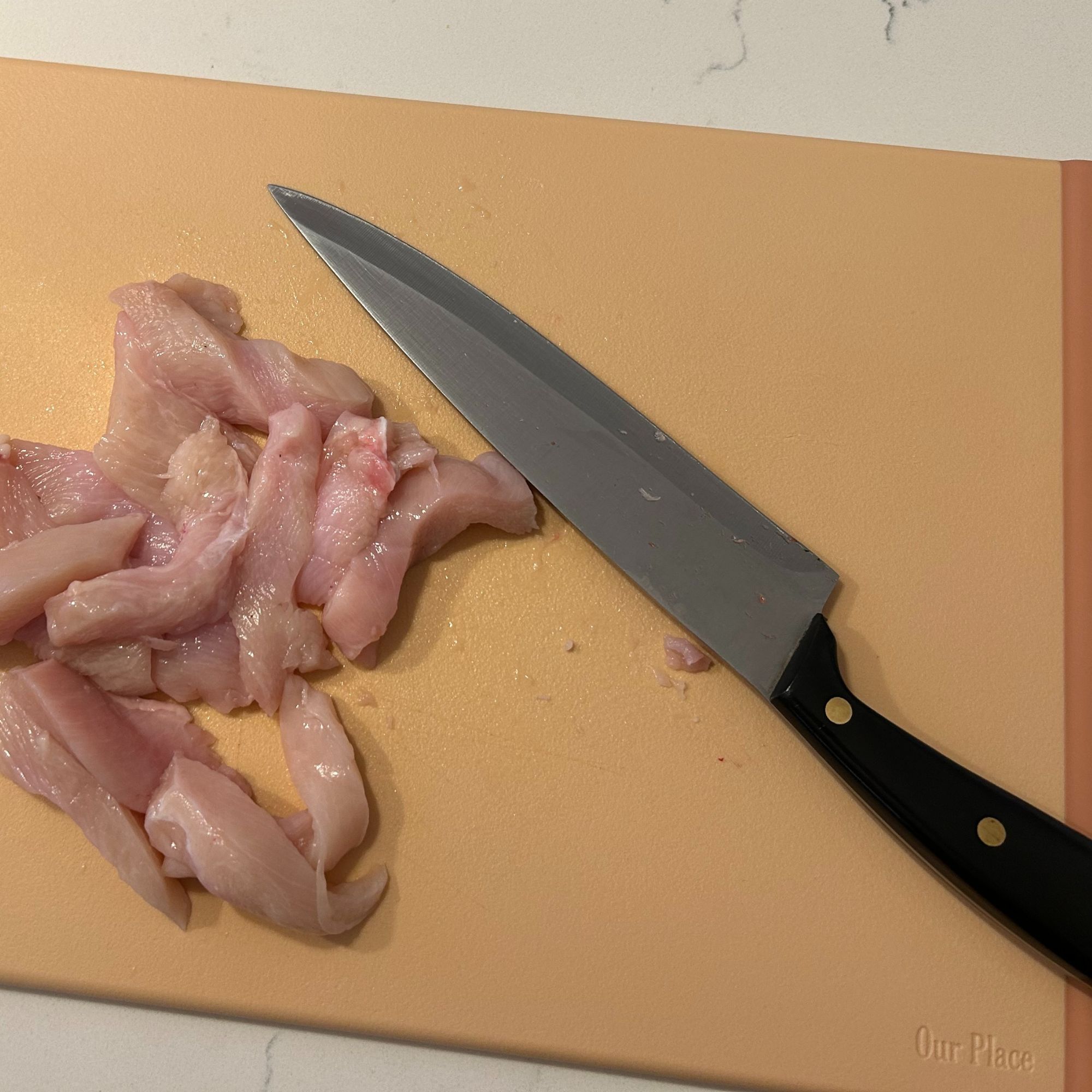 Our Place pink plastic chopping board with raw chicken on and knife