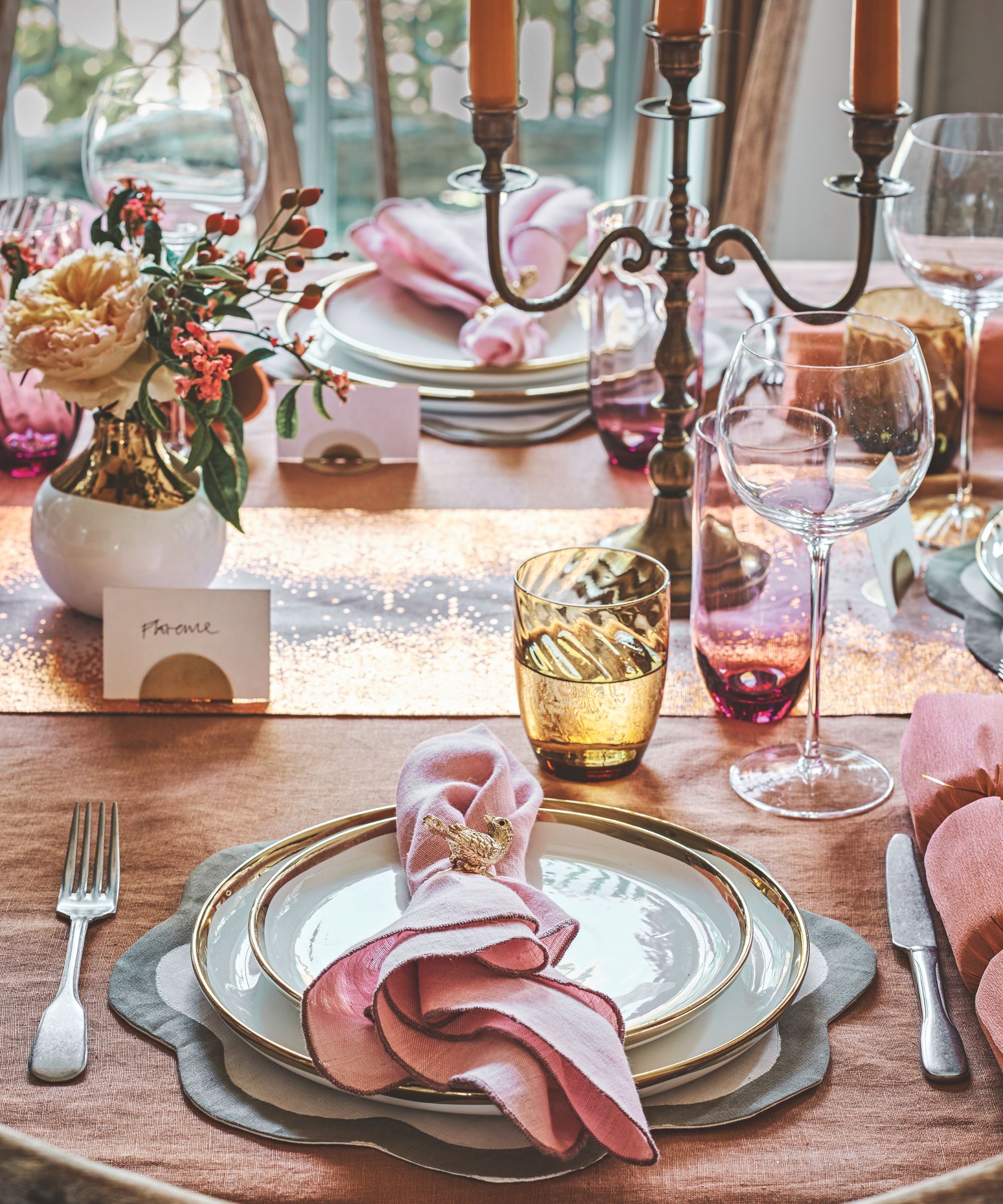 Table setting with white and gold plates, pink napkins, yellow tumblers and pink stemless wine glasses