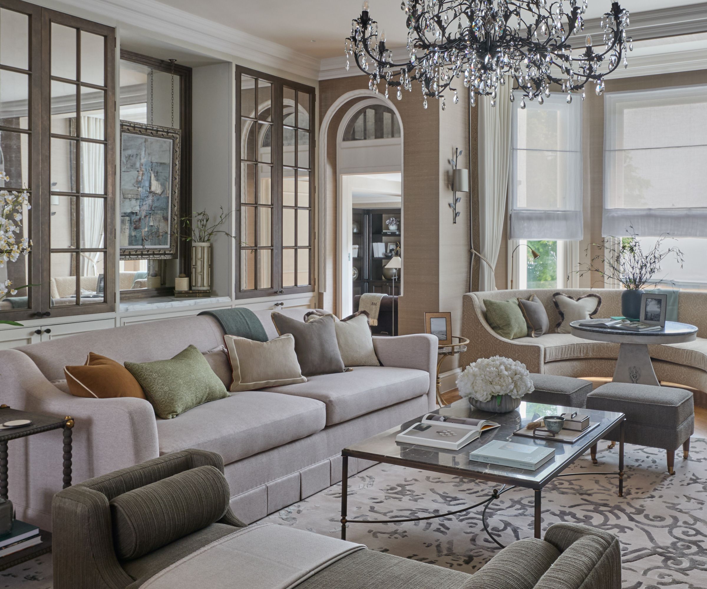 Neutral contemporary livin room with two large crea sofas, green daybed, patterned rug with square glass coffee table, mirrors and windows with blinds and drapes in background
