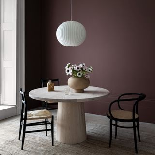 A purple-painted dining room with a round stone dining table and a pendant light