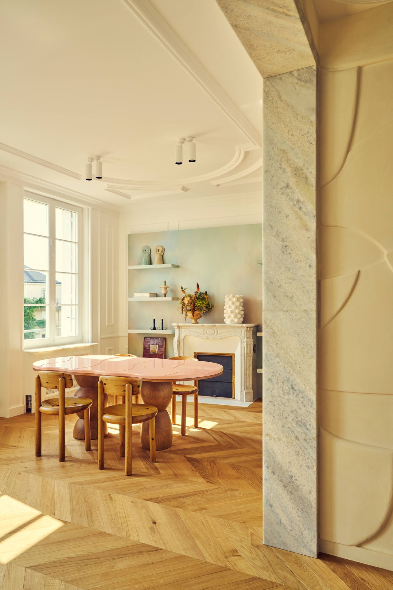 Batiik Studio-designed living room / dining room combo area featuring peachy pastel pinks, herringbone floors, sculptural custom made furniture, and an original fireplace.