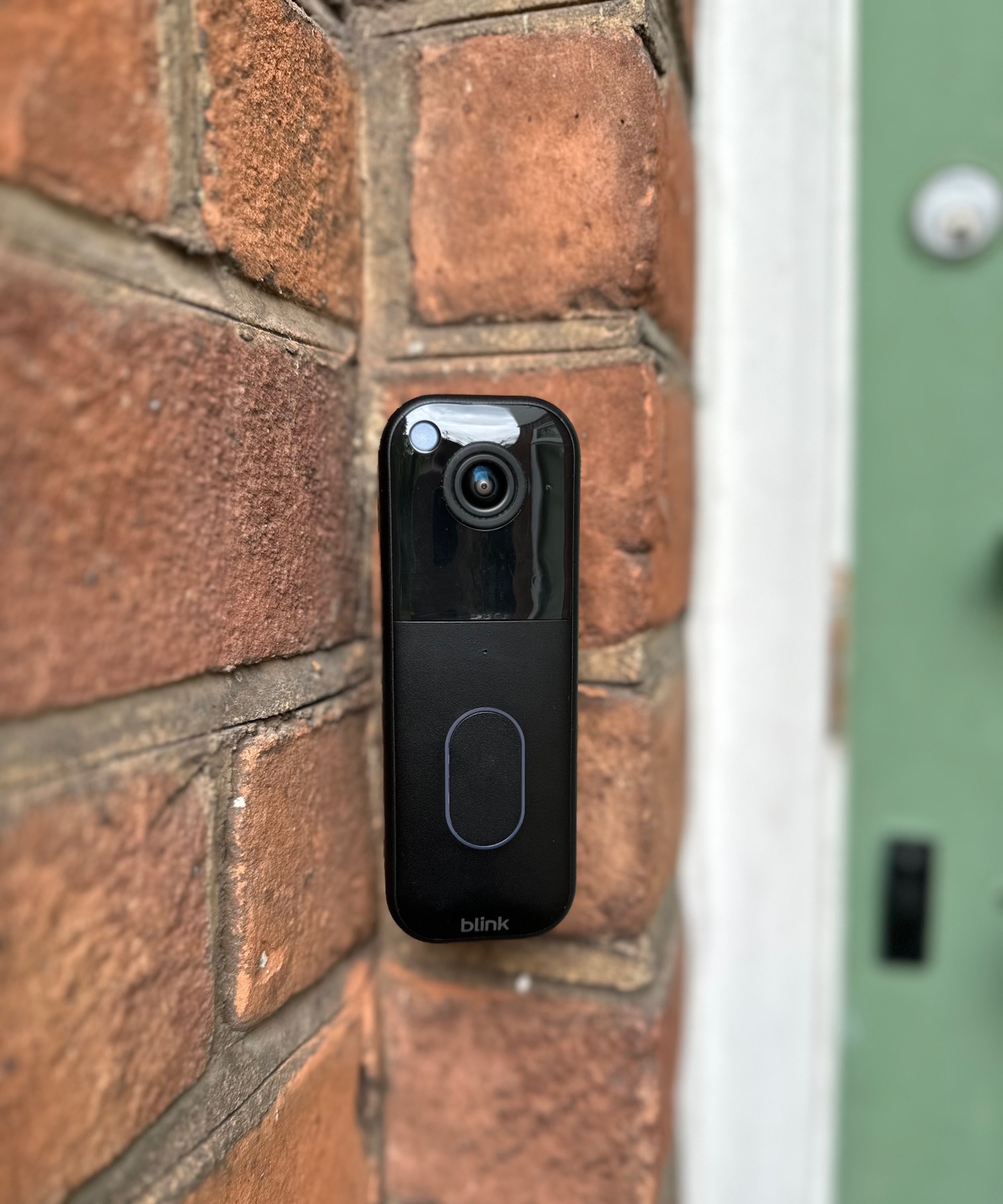 Black Blink Video Doorbell attached to outside wall next to green door