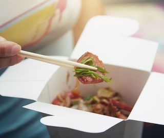 Woman eating Asian fast food from a cardboard box