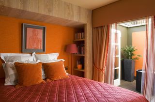 A bedroom painted orange with orange and red soft furnishings