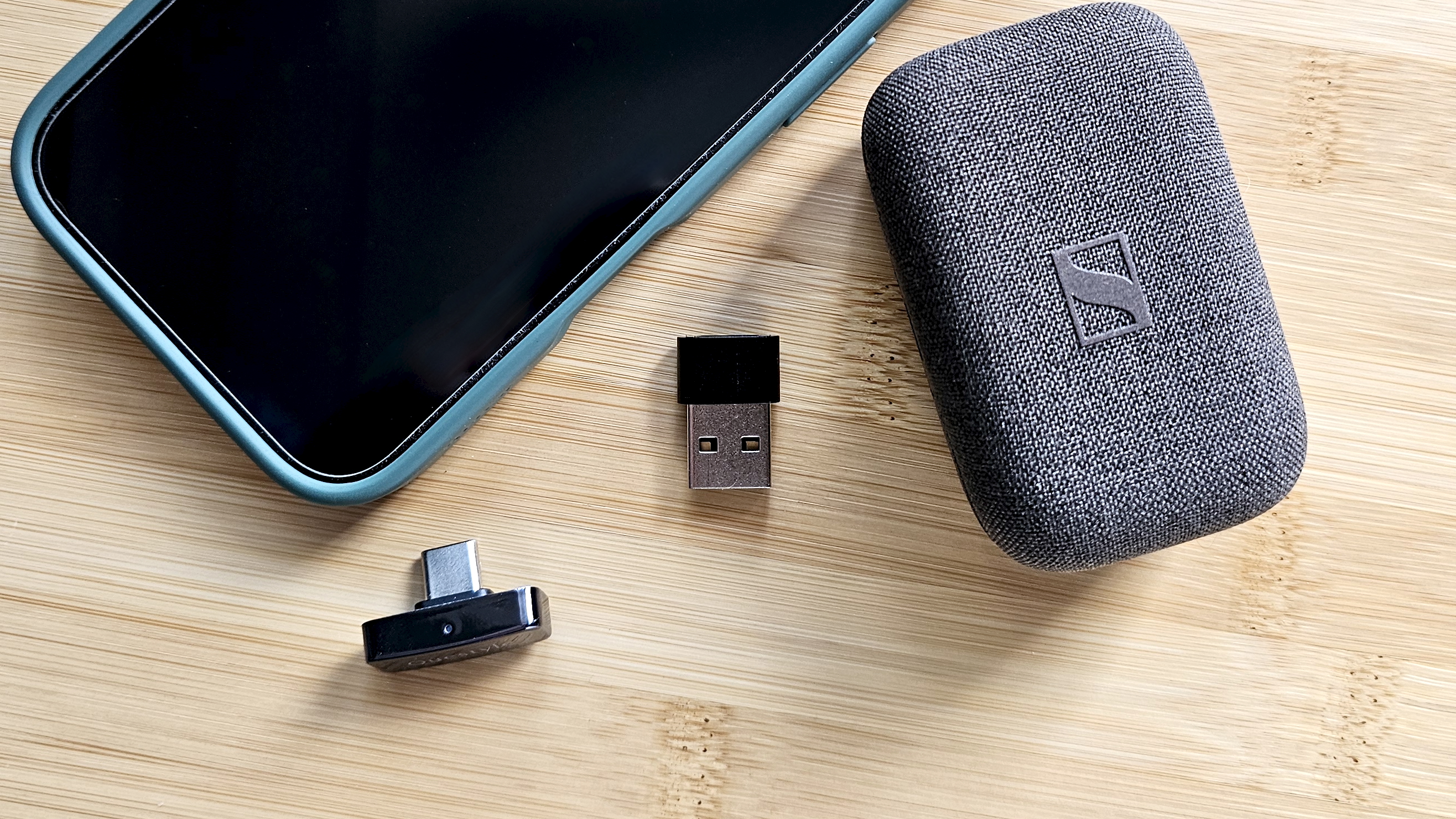The Questyle QCC Dongle Pro with a smartphone to denote size, on a light wooden table