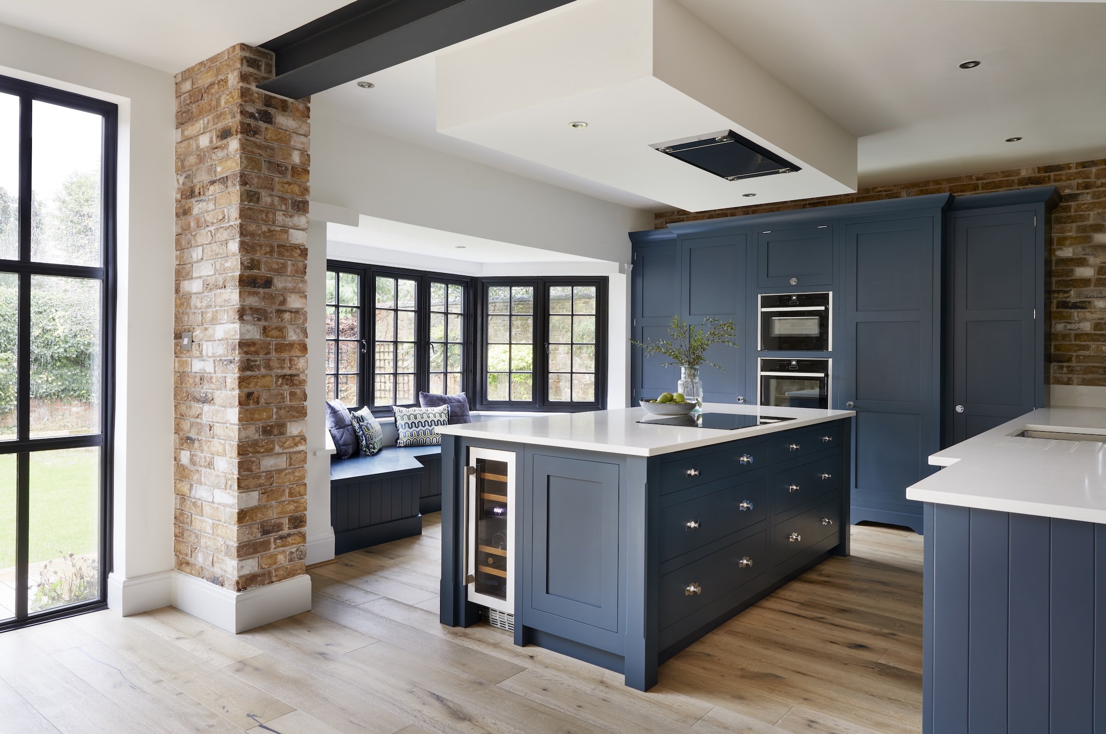 A dark blue kitchen with a bay window and bespoke built in seating