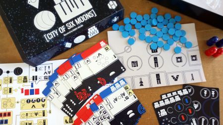 The box, cards, and components of City of Six Moons on a wooden surface, as seen from above