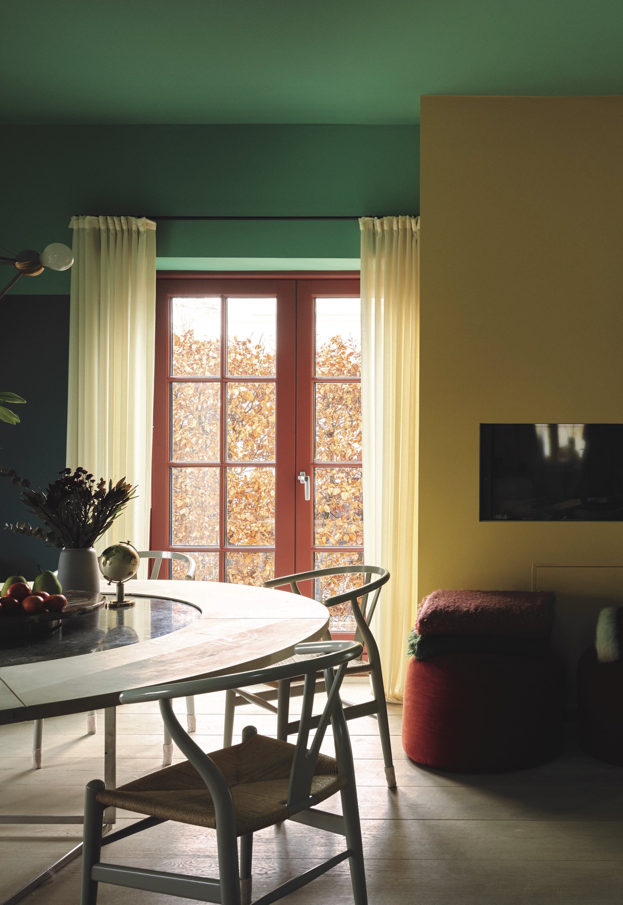 View of a dining room, through to the double doors leading into the garden. The far wall is painted a mint green colour and the wall to the right is a buttercup yellow colour, with the dining table to the left of the space.