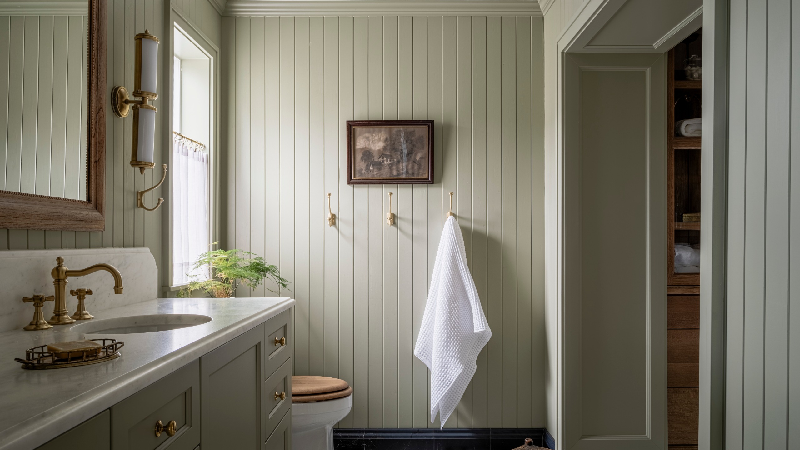 A country bathroom with paneled walls drenched in soft green