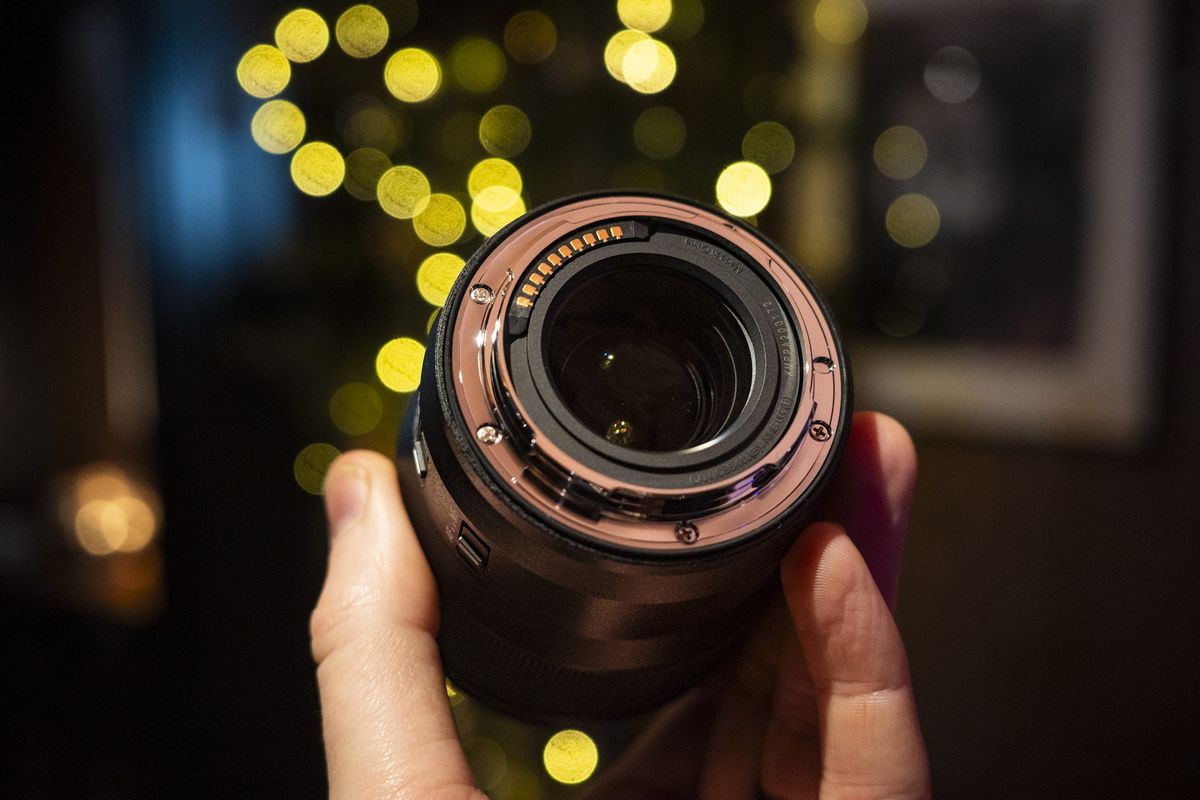 Underside of the Panasonic Lumix S 100mm F2.8 Macro lens in the hand with Christmas lights background