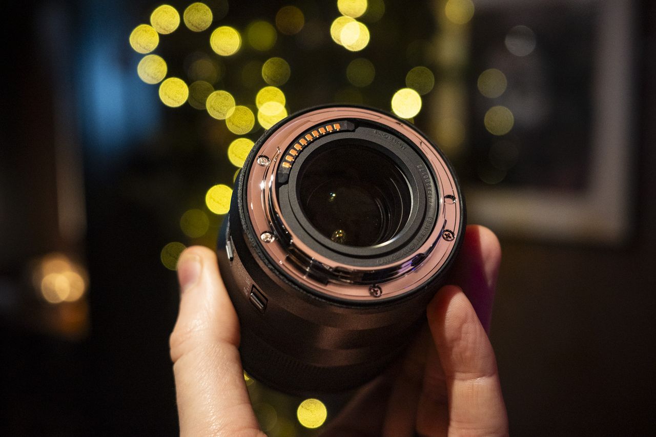 Underside of the Panasonic Lumix S 100mm F2.8 Macro lens in the hand with Christmas lights background