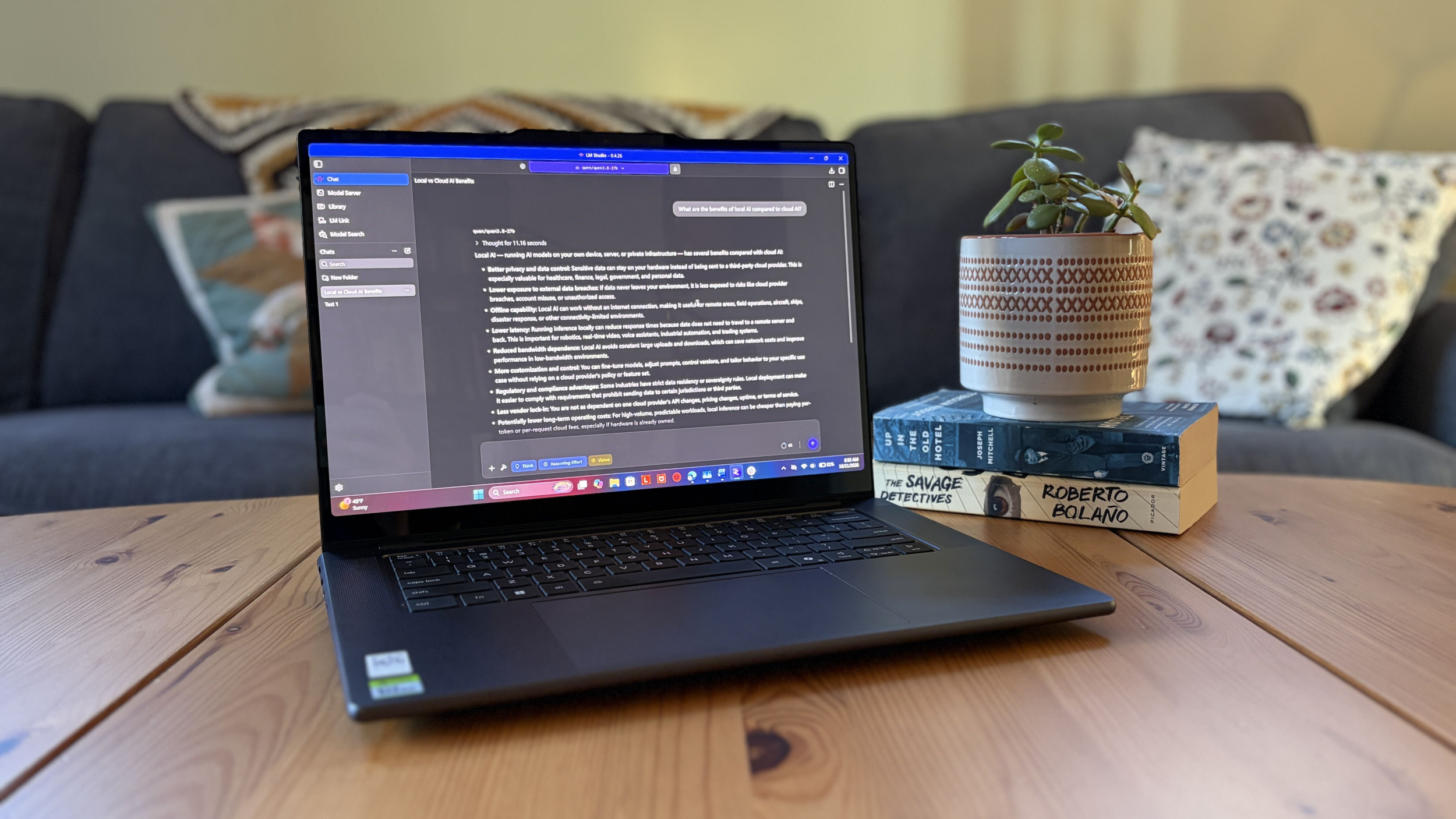 A Lenovo Pro 9n laptop displaying a text-heavy AI workspace sits on a wooden table beside a potted plant on stacked books, creating a calm, cozy living room scene.