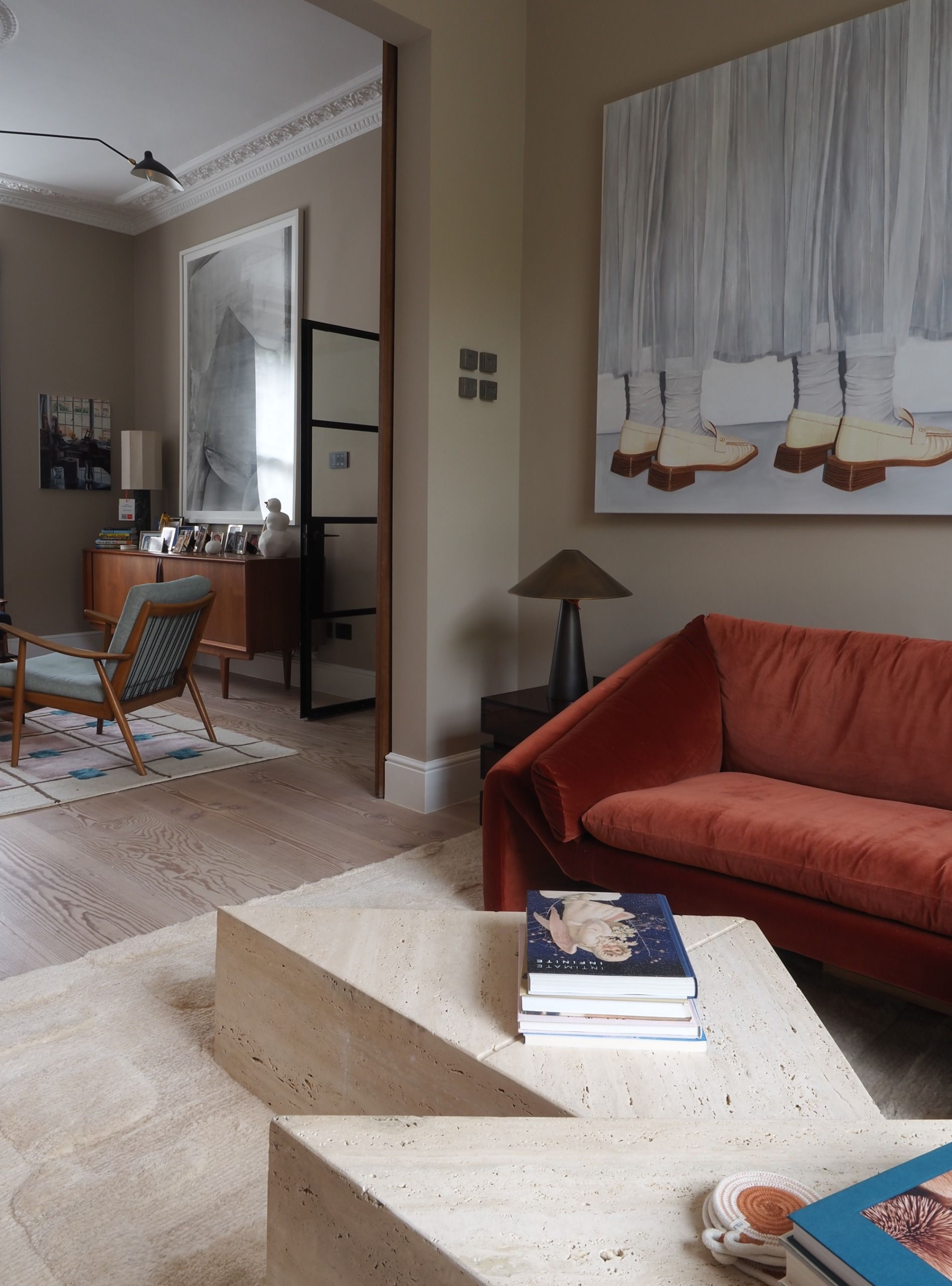 a living room with beige walls, wall art, a red sofa and a view through another sitting room