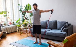Man watching online videos and doing exercise with resistance bands at home