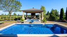 A large in-ground swimming pool, with a raised hot tub behind it. A concrete pagoda beyond, surrounded by trees.