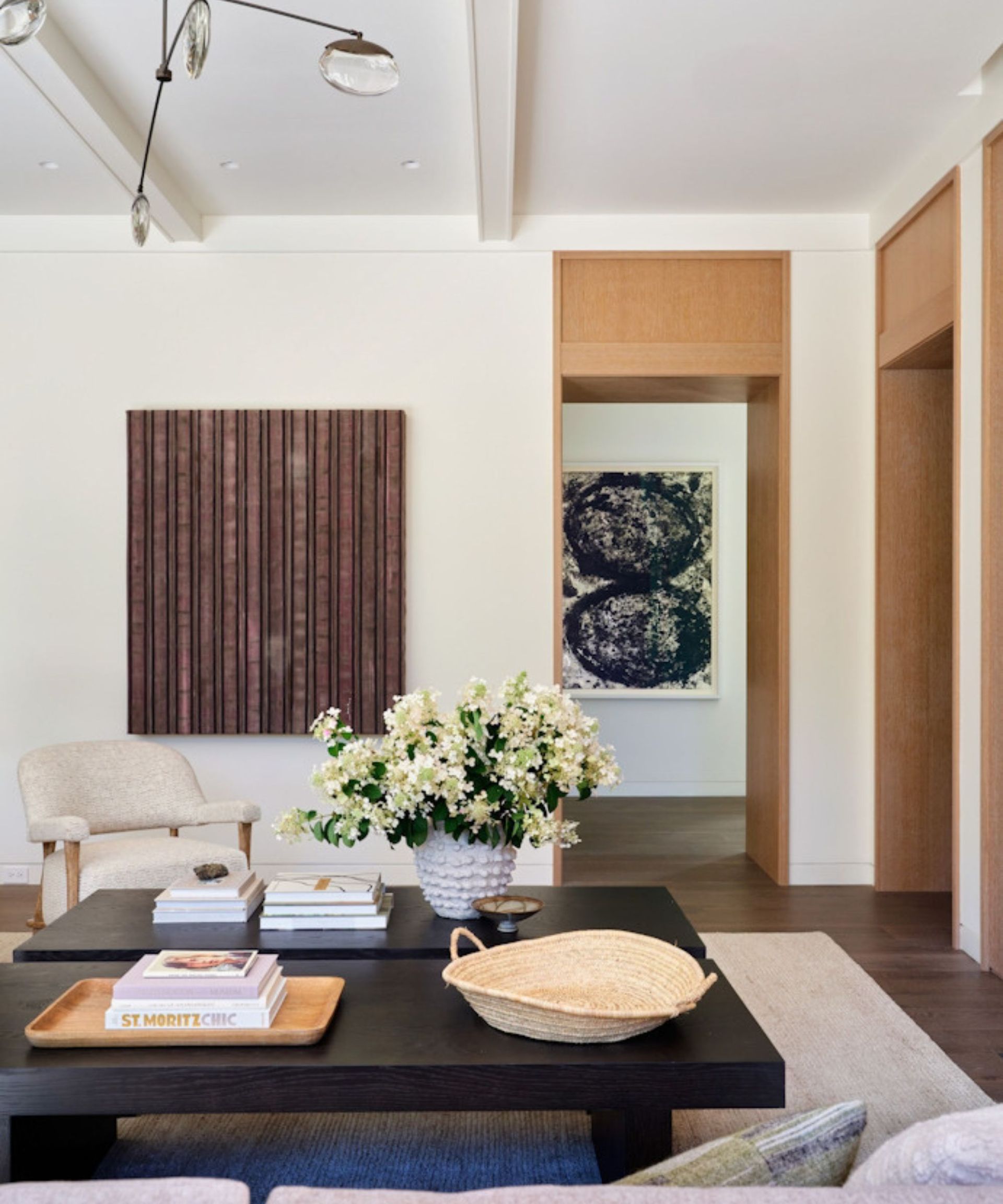 white living room with modern decor, black coffee table, abstract artwork, neutral rug with neutral armchair