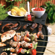 BBQ food on grill and sweetcorn cobs on white plate