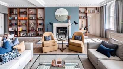 A blue living room with white fireplace, walnut bookshelves and yellow armchairs 