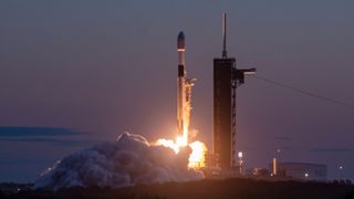 a black and white rocket launches into a darkening evening sky