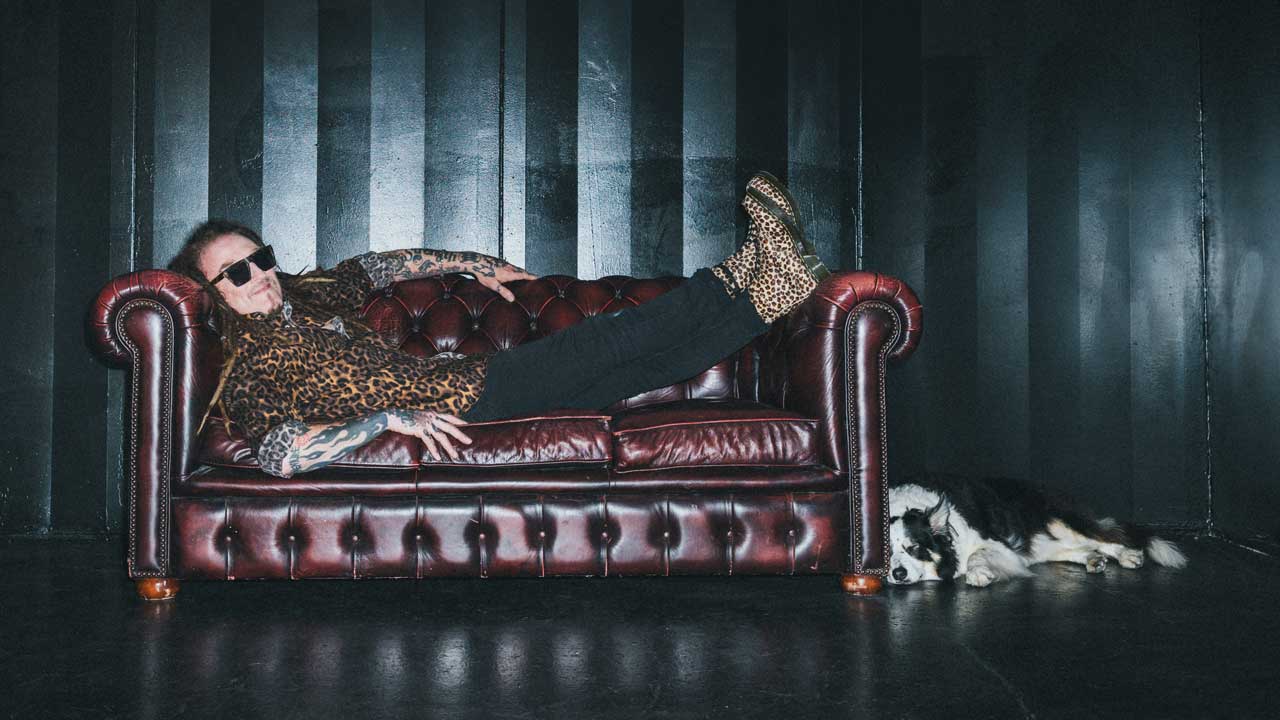 Ginger Wildheart reclining on a Chesterfield with his dog 