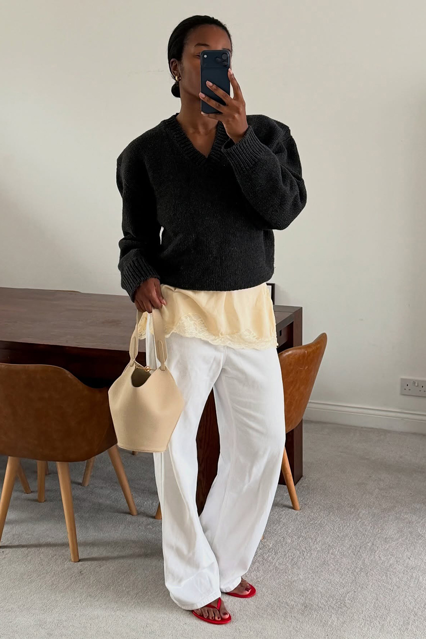 A woman wearing a black sweater, white jeans and red flip flops