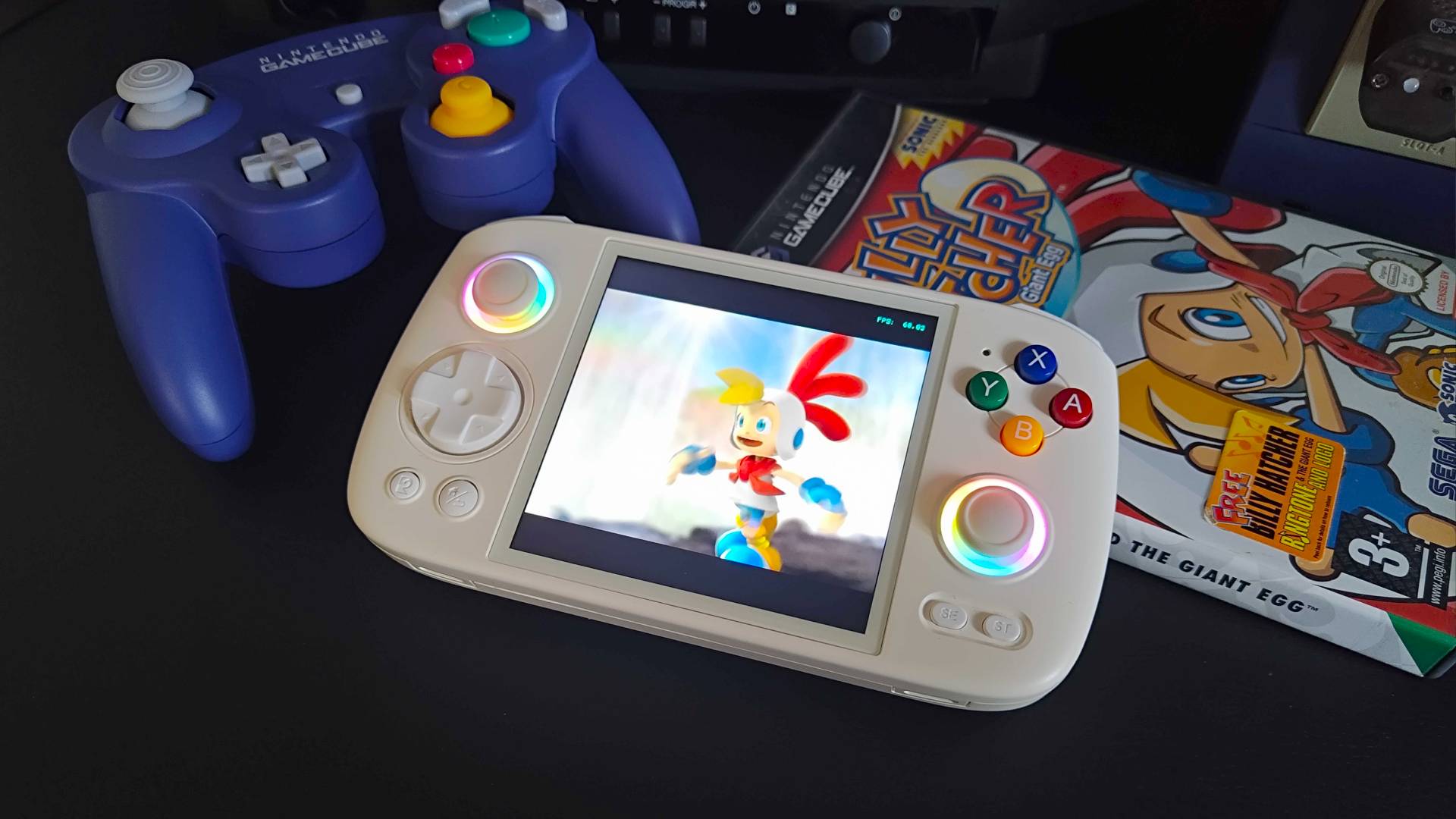 Anbernic RG Cube on black desk next to GameCube controller and Billy Hatcher and the Giant Egg game box.