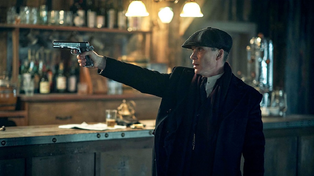 Tommy Shelby i Netflix-serien Peaky Blinders, som står og sigter på nogen med en pistol i en bar.