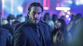 A rain soaked John Wick searches for someone in a neon setting as part of our John Wick movies in order guide