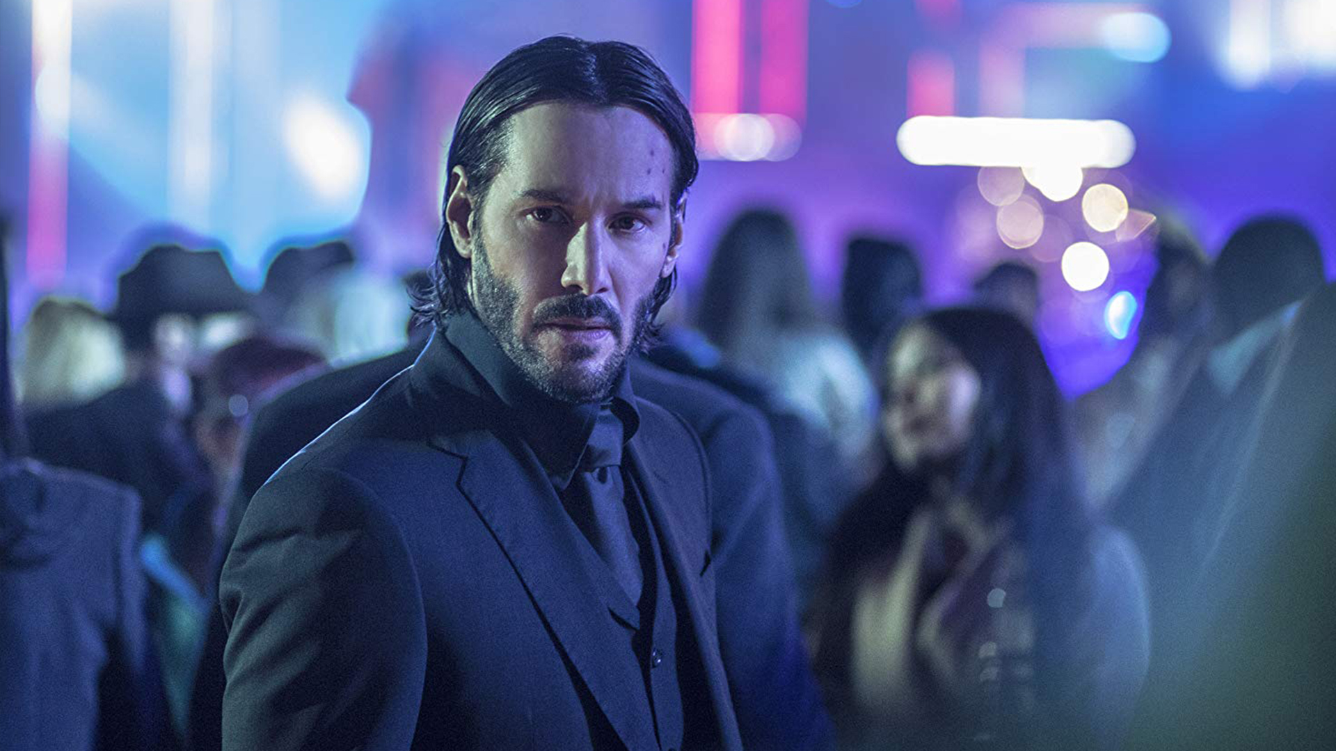 John Wick in a sharp suit is looking for someone in a neon scenery in one of his films