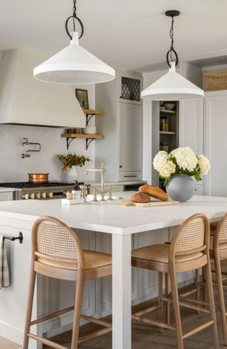 Modern kitchen with kitchen island, rattan style bar stools, two low hanging white pendants