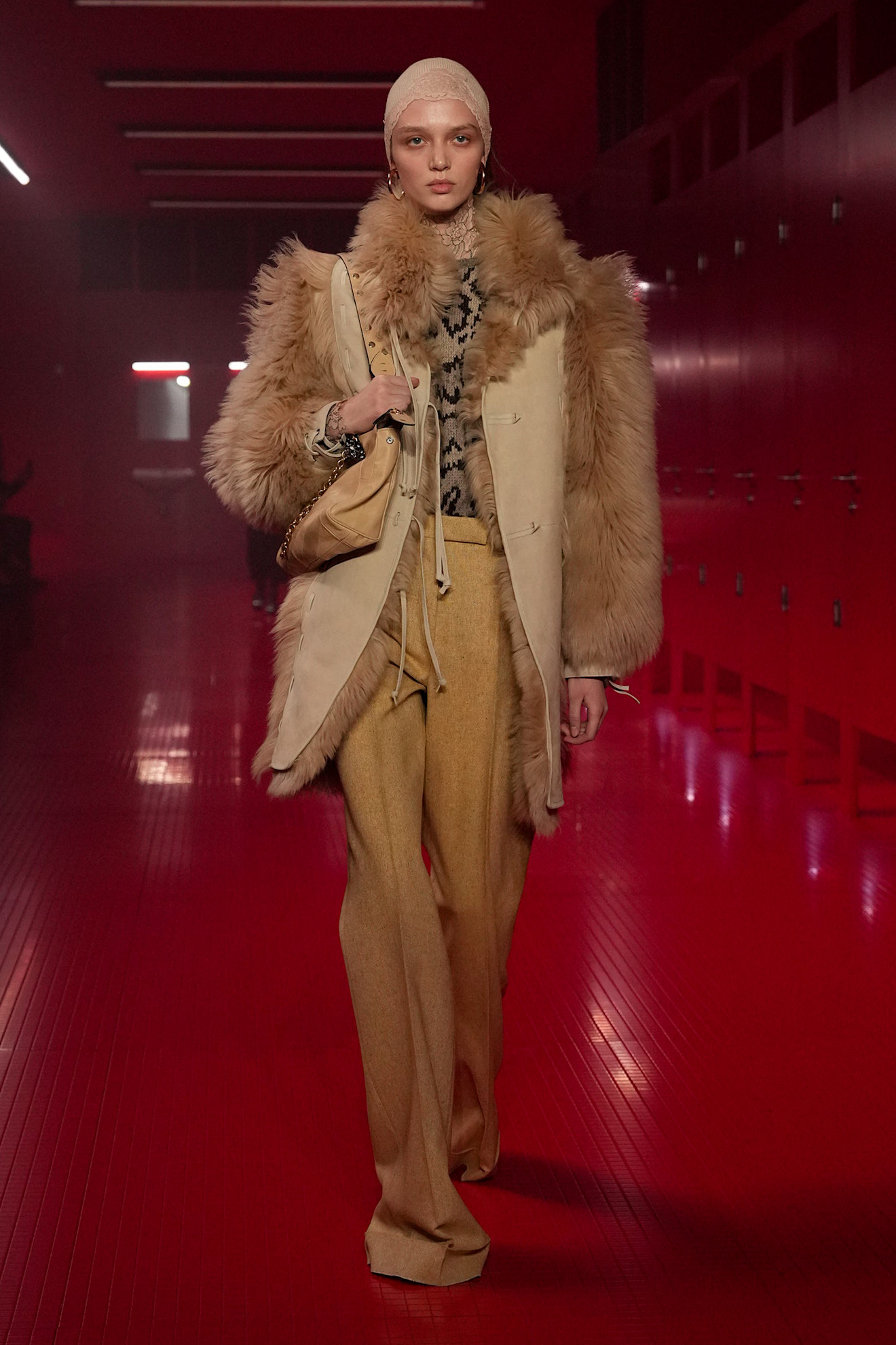 Um modelo andando no show F/W 25 Valentino durante a Paris Fashion Week, vestindo um casaco de pele bronzeado com uma blusa estampada e calças de mostarda.