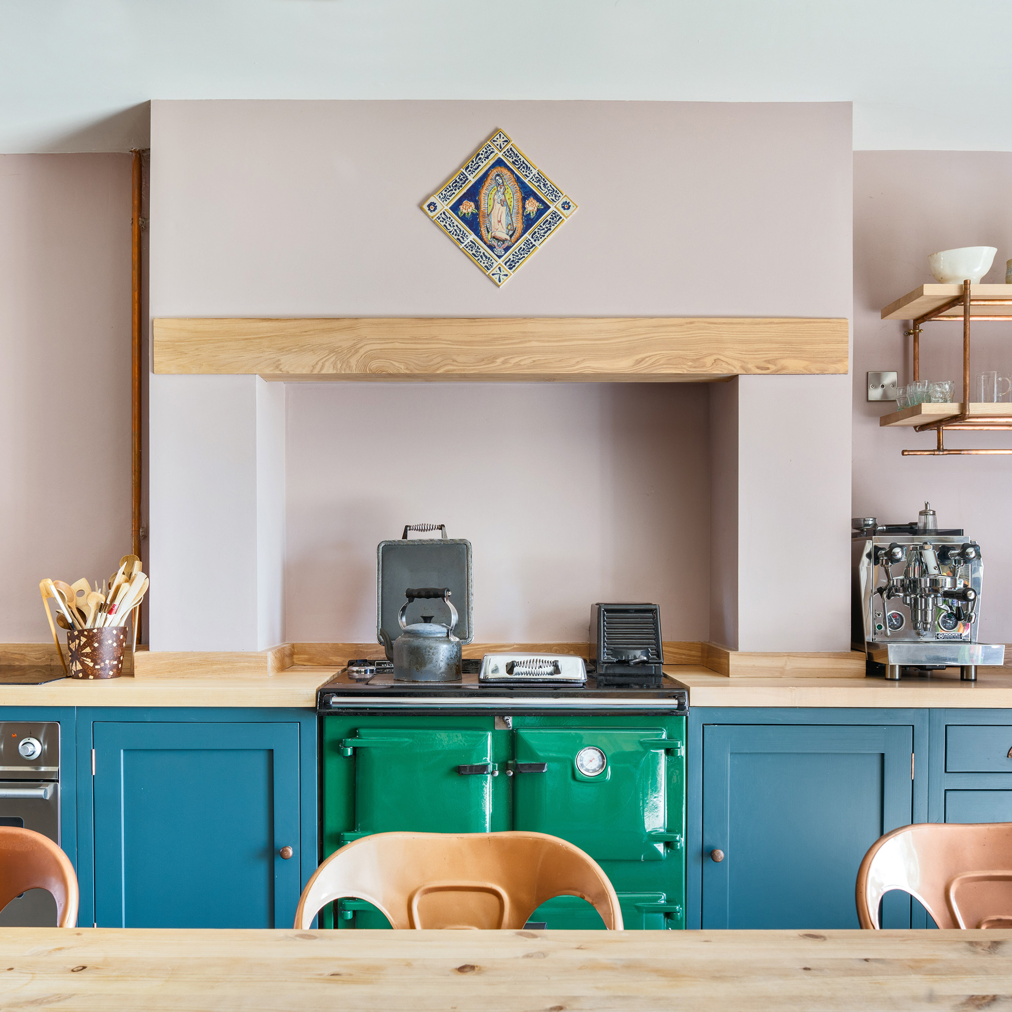 pink walls in kitchen with ash worktops and green range cooker with blue painted cabinets in a country kitchen