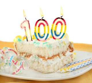 A piece of birthday cake, with a "100" candle on top.